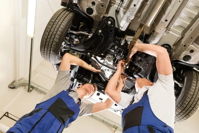 Two mechanics are repairing a car from downside of a uplifted car on car lift in garage