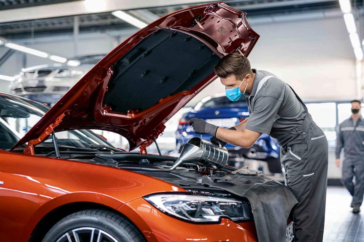 A mechanic is filling oil in BMW car in a garage