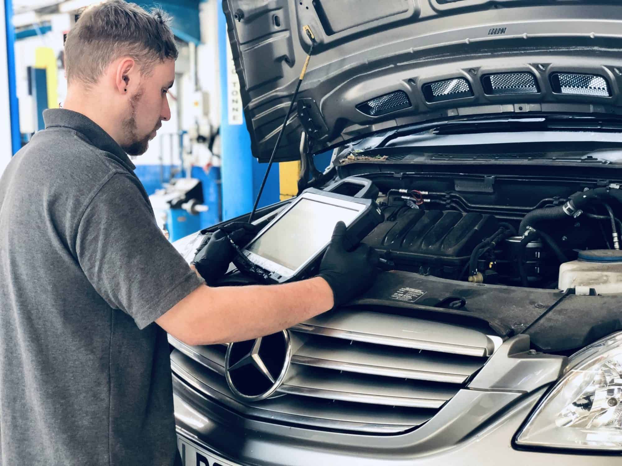 A mechanic is inspecting Mercedes Benz car through diagnostic scanner