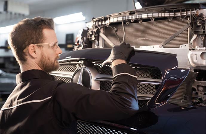 A mechanic is fixing front body part of a Mercedes Benz car