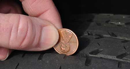 A person using a coin to measure the depth of their tire tread