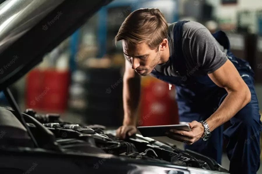 Young auto repairman analyzing car engine breakdown while using digital tablet repair shop